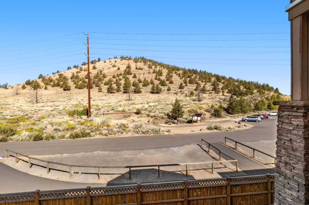 Balcony overlooking parking lot, street, and large desert hill with foliage and powerlines