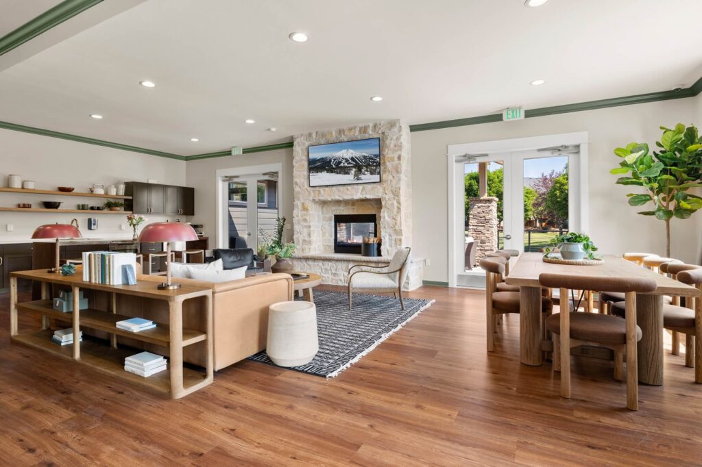 Clubhouse interior with lounge seating around a fireplace with television mounted above it next to a kitchen and dining space